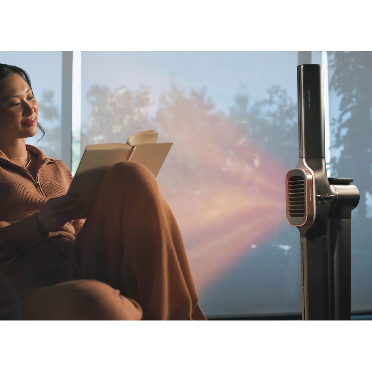 Une femme lit dans son fauteuil, réchauffée par le Shark TurboBlade Cool + Heat anthracite en mode Confort