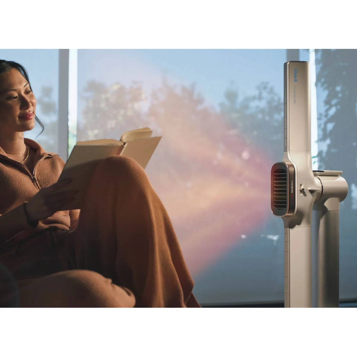 Une femme lit dans son fauteuil, réchauffée par le Shark TurboBlade Cool + Heat en mode Confort
